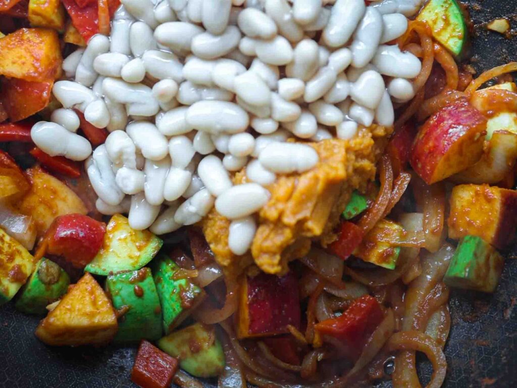 adding cannellini beans to pan of veggies for curry